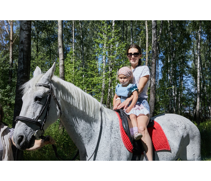 Мама с дочкой фотографируется во время катания на лошади.